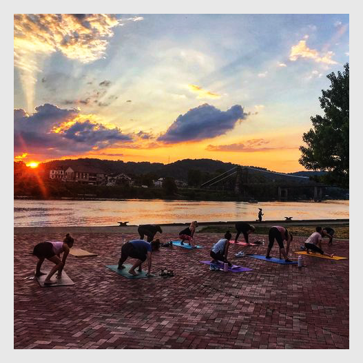 Wheeling: group of people practicing yoga at sunset along the water.